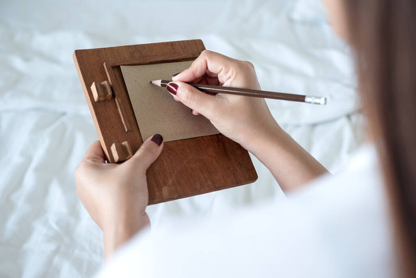Μια γυναίκα που γράφει σε καφέ χαρτί με ξύλινο σημειωματάριο στο κρεβάτι. - Φωτογραφία, εικόνα