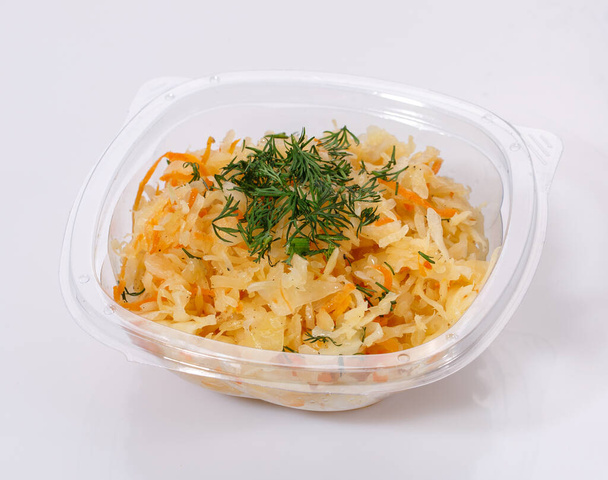 Salade traditionnelle de chou-fleur, carottes, oignons et aneth dans un bol en plastique transparent sur fond blanc. - Photo, image