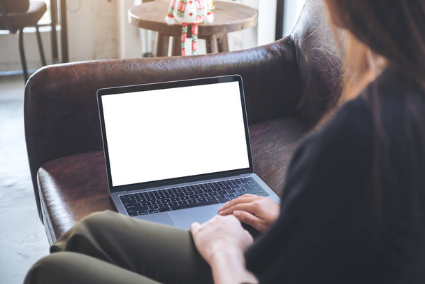 Mockup obraz kobiety korzystającej i patrząc na laptopa z pustym białym ekranem pulpitu podczas siedzenia na kanapie - Zdjęcie, obraz