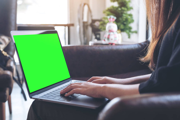 Image de maquette de femme utilisant et tapant sur un ordinateur portable avec écran de bureau vert vierge et tasses à café sur la table dans un café loft moderne - Photo, image