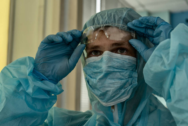 Müder Arzt zieht nach Feierabend seinen Schutzanzug aus - Foto, Bild