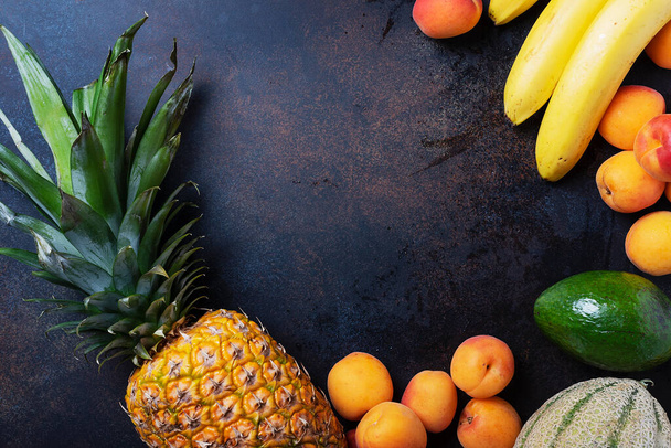 Concept van gezond veganistisch voedsel. Ananas, banaan, abrikoos, meloen, avocado op zwarte achtergrond. Bovenaanzicht afbeelding - Foto, afbeelding