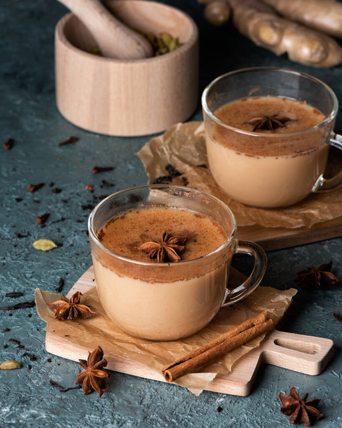 Glass cups of traditional Indian masala chai on dark green texture background. Ingredients of beverage black tea, ginger, cinnamon, cardamom, anise stars - Foto, Bild
