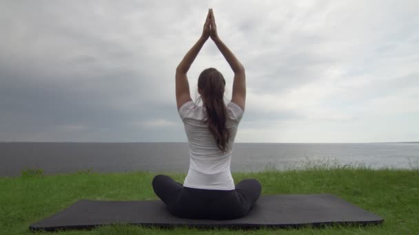 若いフィット女性は湖や海の近くの海岸でヨガを練習します。蓮のポーズで座って瞑想する女性 - 映像、動画