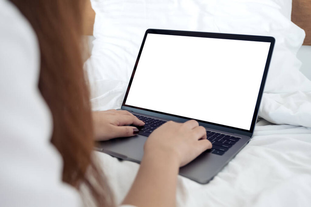 Mockup obrázek ženy sedící na posteli, pomocí a psaní na notebooku s prázdnou bílou desktopovou klávesnicí  - Fotografie, Obrázek
