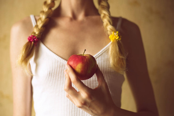 Piros alma női kézben. Fiatal lány copfos fehér felsőben - Fotó, kép