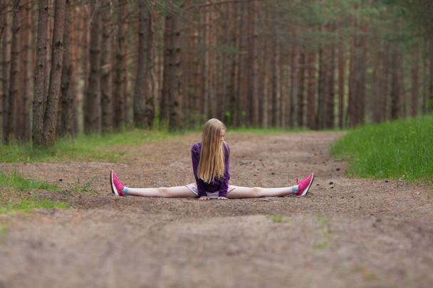 Flexible girl doing the splits in the pine forest. Gymnastics on fresh air far away from people. Stay in fit during quarantine. Active and healthy  lifestyle concept. - Photo, Image