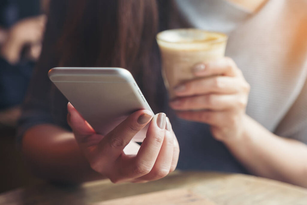 Крупный план женской руки, держащей и использующей смартфон во время питья кофе в кафе
 - Фото, изображение