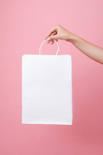 white paper bag under the logo in the hands of the girl on a pink background. Shopping - Foto, Imagem