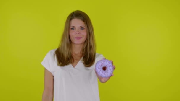 Frau im weißen T-Shirt hebt Hand mit blauem Donuts in die Kamera, lächelt - Filmmaterial, Video