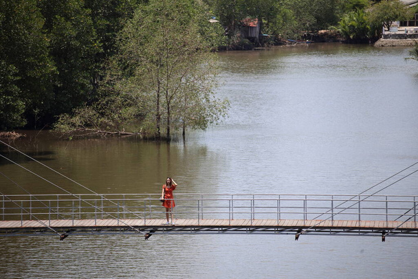 A woman standing on a wooden walkway at Rak samae Bridge in Rayong, Thailand - 写真・画像