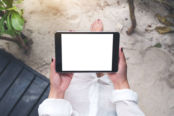 Kum ve plaj arka planına sahip boş beyaz masaüstü ekranlı siyah tableti tutan bir kadının el resmi. - Fotoğraf, Görsel