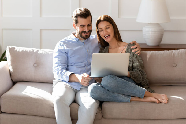 Happy couple using laptop together, relaxing on cozy couch - Foto, imagen
