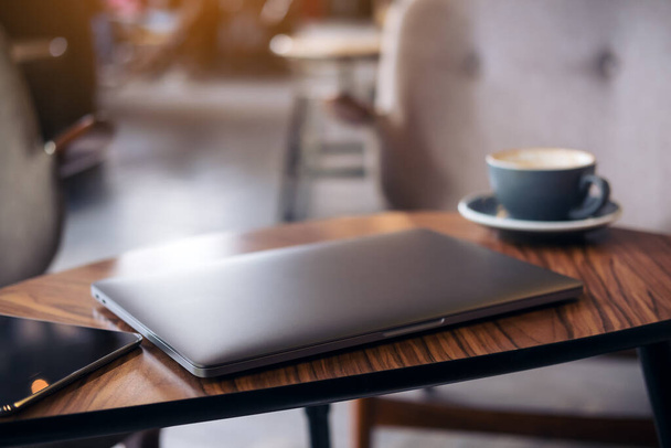 Imagen de primer plano de la computadora portátil de color plata, PC tableta y taza de café en la mesa de madera con fondo borroso café
 - Foto, imagen