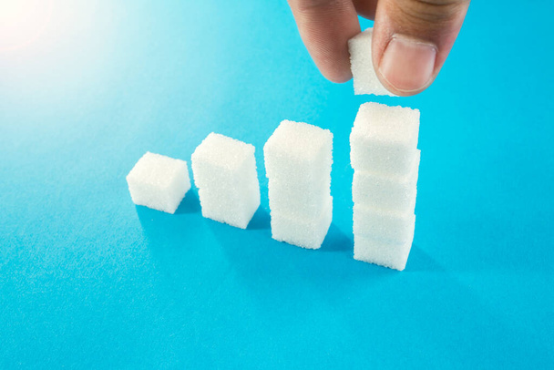 degree of sugar cubes on a blue background man's hand makes a cube. diabetes mellitus. - Valokuva, kuva