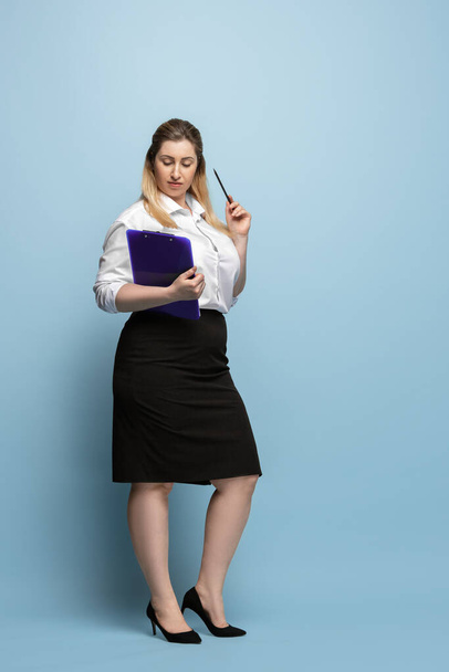Mulher caucasiana jovem no escritório traje em fundo azul. Personagem feminina positiva para o corpo. mulher de negócios plus size
 - Foto, Imagem