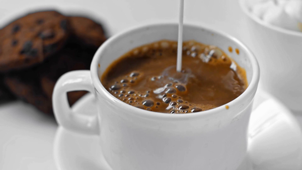 close-up van verse melk gieten in kopje zwarte koffie op wit  - Video