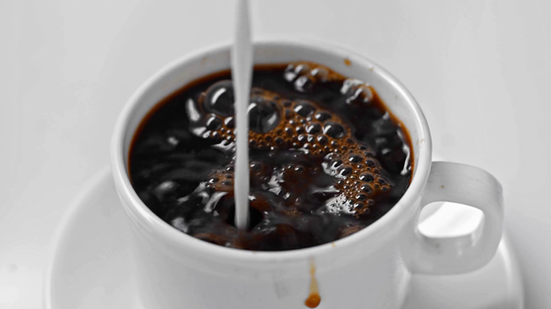 close up of milk pouring in cup of black coffee isolated on white  - Footage, Video