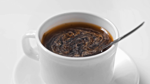 czarna kawa w filiżance z wyizolowaną łyżką na białym - Materiał filmowy, wideo