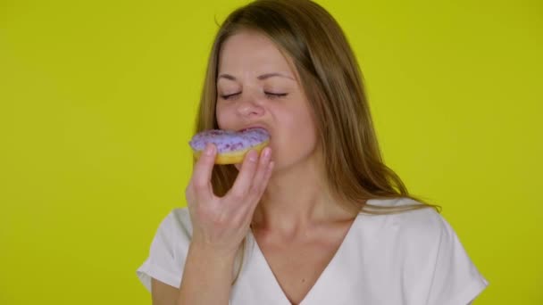 Frau im weißen T-Shirt beißt zu, isst leckere blaue Donuts, genießt den Geschmack - Filmmaterial, Video