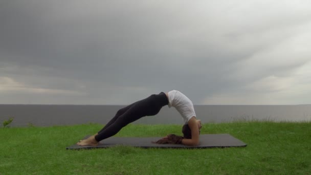 Junge, fitte Frauen praktizieren Yoga an der Küste in der Nähe des Sees oder Meeres. Frau macht Inverted Staff Dvi Pada Viparita Dandasana Pose - Filmmaterial, Video
