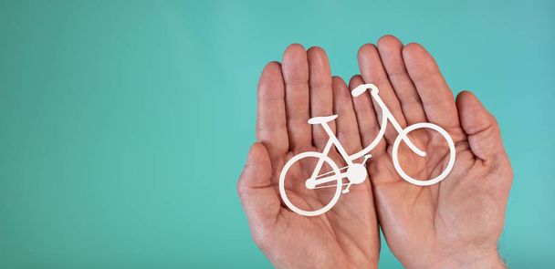 Concepto de seguro de bicicleta con bicicleta de papel en las manos sobre fondo de color turquesa
 - Foto, Imagen