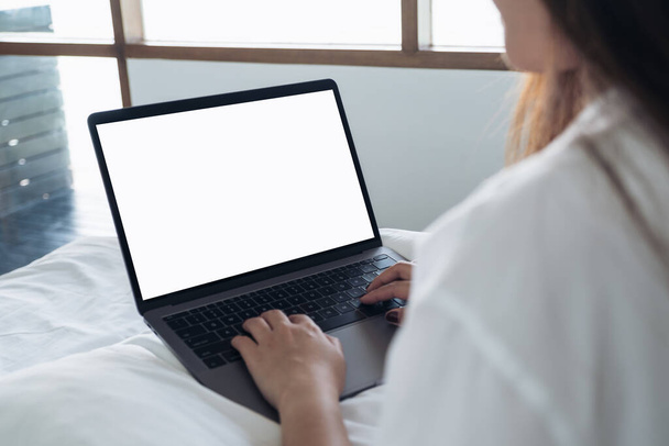 Yatakta oturan Asyalı bir kadının boş beyaz masaüstü klavyesi olan dizüstü bilgisayarı kullanarak ve yazarak görüntüsü.  - Fotoğraf, Görsel
