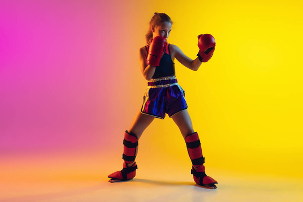 Little caucasian female kick boxer training on gradient background in neon light, active and expressive - Foto, afbeelding
