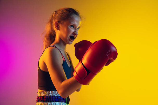 Little caucasian female kick boxer training on gradient background in neon light, active and expressive - Foto, imagen