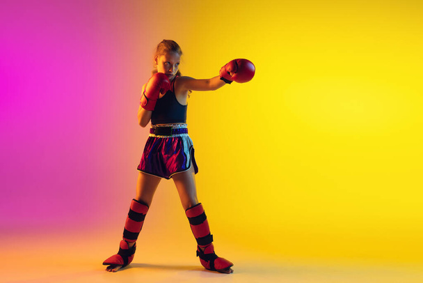 Little caucasian female kick boxer training on gradient background in neon light, active and expressive - Photo, Image