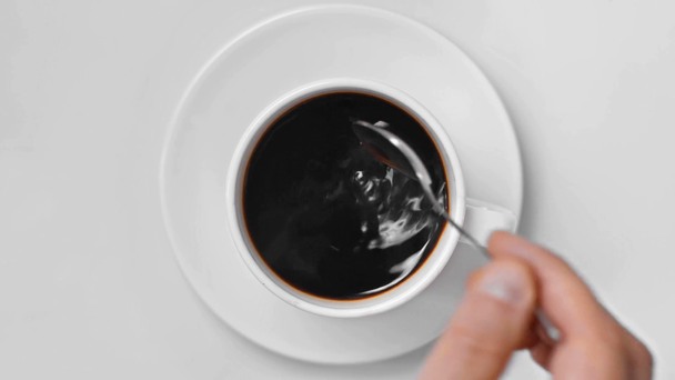 widok z góry człowieka mieszając czarną kawę z łyżką na białym - Materiał filmowy, wideo