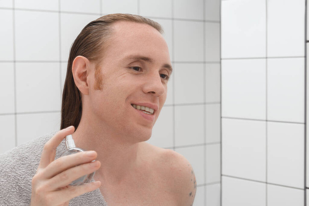 Mężczyzna z tatuażami i lakierem do włosów na twarzy po goleniu w łazience - Zdjęcie, obraz