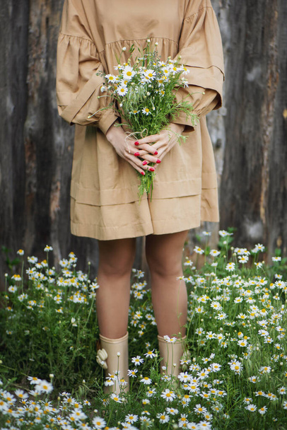 Woman holding bouquet of chamomile in hands near the fence. - Foto, Imagen
