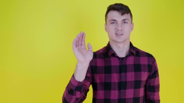 Man heft hand, toont palm aan de camera en zegt stop op een gele achtergrond - Video