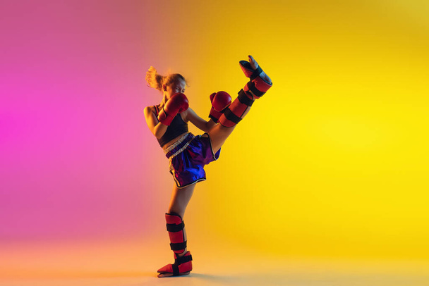 Little caucasian female kick boxer training on gradient background in neon light, active and expressive - Photo, Image