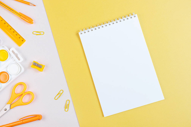 Concept back to school. School stationery flat lay: notepad with blank page, pens, pencils, sharpener, scissors, ruler, paper clips on yellow and gray background. Orange and yellow tones. Copyspace. - Photo, Image