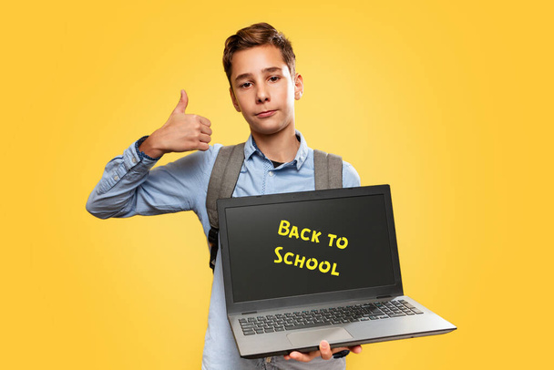 Concept of modern technologies and education. Caucasian teen boy holding open laptop and showing thumbs up. Yellow background. Copy space. Back to school - Fotografie, Obrázek