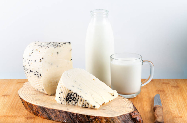 Τυρί με μαύρο κύμινο σπόρους με μπουκάλι γάλα σε ξύλινο φόντο. - Φωτογραφία, εικόνα