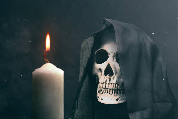 Human skull with a black cloak and burning candle on dark background. Halloween concept - Fotoğraf, Görsel