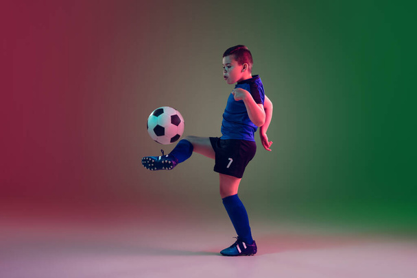Teen male football or soccer player, boy on gradient background in neon light - motion, action, activity concept - Fotó, kép