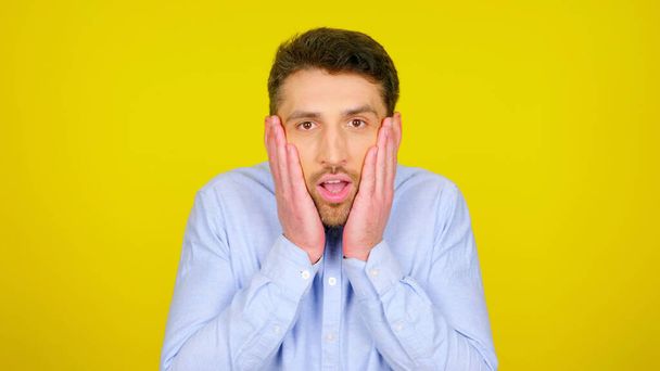 Surprised man in a light blue shirt on a yellow background with copyspace - Photo, Image