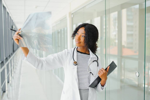 Portrait confident African American female doctor medical professional writing patient notes isolated on hospital clinic hallway windows background. Positive face expression - Fotografie, Obrázek