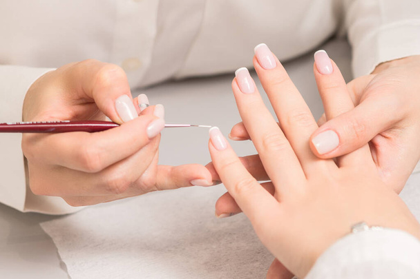 Dłoń młodej kobiety otrzymującej francuski manicure od kosmetyczki w salonie kosmetycznym. - Zdjęcie, obraz