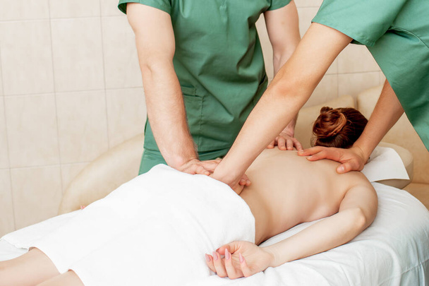 Rückenmassage der Frau in vier Händen durch zwei Masseure im Massagesalon. - Foto, Bild