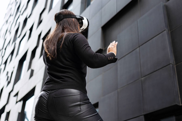 Back Of Woman Wearing Virtual Reality Technology Glasses Against Modern Building - Foto, Imagen
