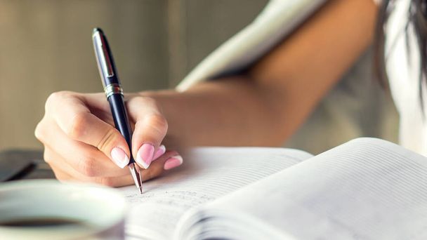 Молодая женщина правой рукой пишет планы на небольшой дневник в кафе крупным планом. Концепция бизнеса
 - Фото, изображение