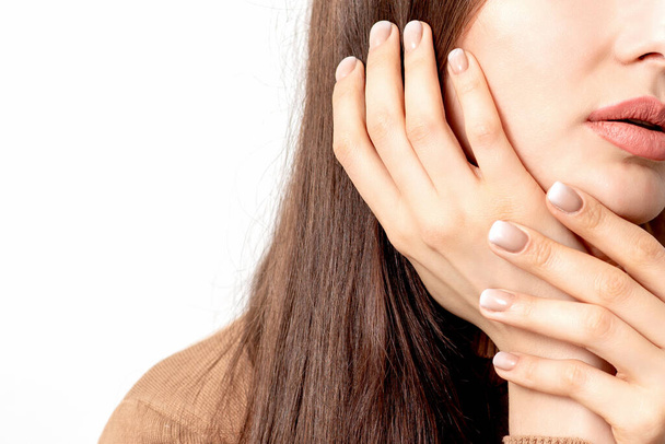 Portrait of pretty young woman touching face with her hand beige manicure on white background with copy space. - Foto, afbeelding