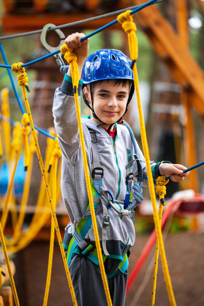 Young boy climbing pass obstacles in rope. Child in forest adventure park. Kids climb on high rope trail. Agility and climbing outdoor amusement center for children. - Foto, Imagem