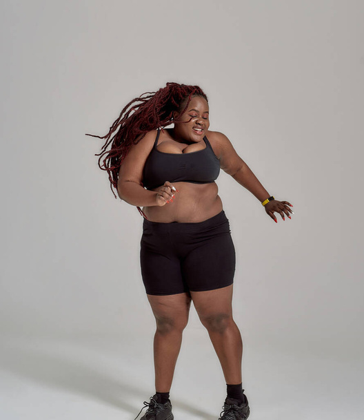 My body none of your business. Plump, plus size african american woman in sportswear having fun, dancing in studio over grey background - Фото, зображення