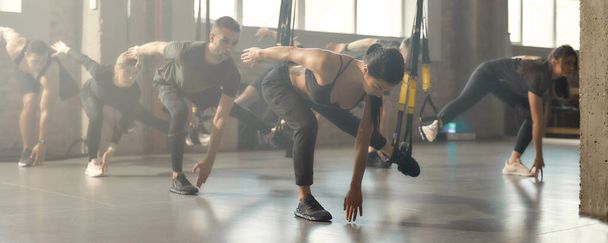 Knockout Fitness. Foto completa de hombres y mujeres haciendo ejercicios de entrenamiento de fitness en el gimnasio industrial. Correas, concepto de entrenamiento en grupo
 - Foto, imagen